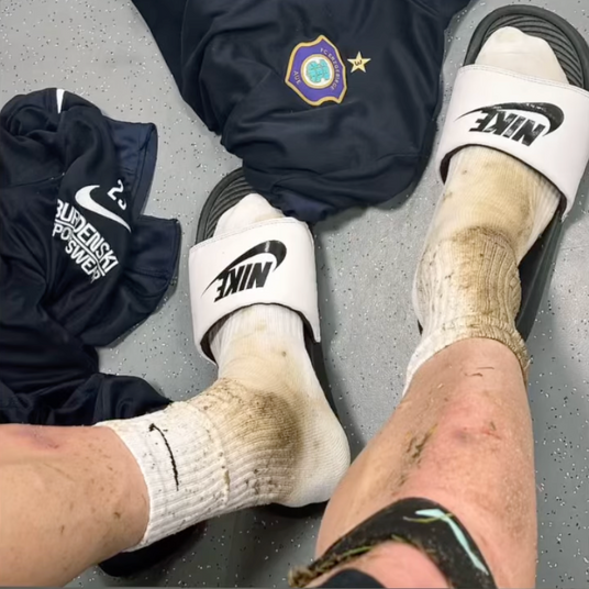 Nach dem Spiel: Fußballspieler in der Kabine mit verschmutzten Socken und neolevee Bandage – sichtbarer Einsatz, authentischer Moment sportlicher Leidenschaft.